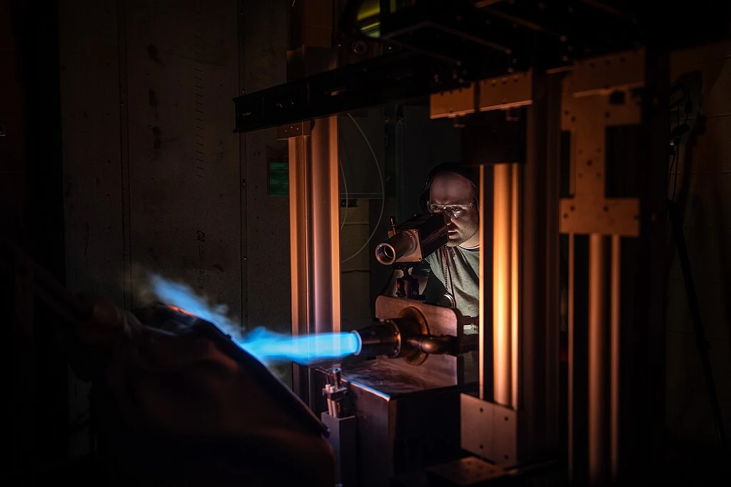 NASA Glenn’s Natural Gas/Oxygen Burner Rig is used to study the high temperature performance of various metal alloys, ceramics, and protective coatings for aero and space propulsion systems. The burner rig provides an easily accessible and economical method to simulate engine operating conditions to understand thermomechanical and thermochemical degradation of materials and structures. In the photo, Materials Research Engineer Michael Presby uses an infrared pyrometer to monitor the surface temperature of the material.