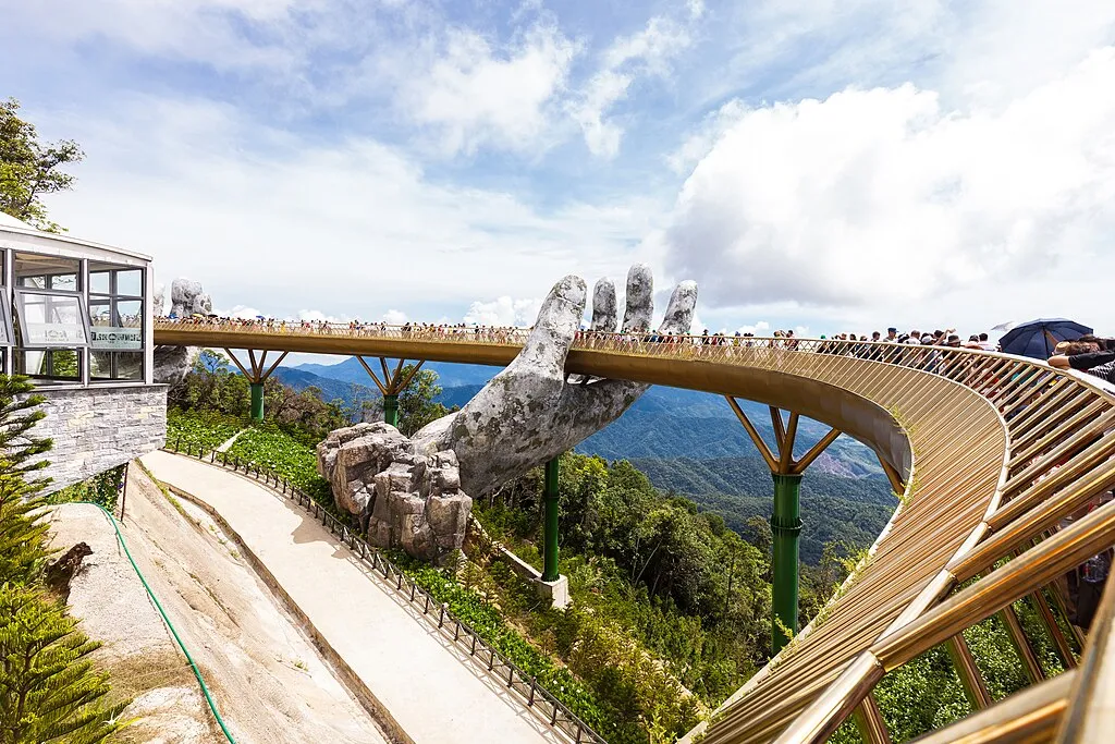The Golden Bridge is a 150-metre-long (490 ft) pedestrian bridge in the Bà Nà Hills resort, near Da Nang, Vietnam.It is designed to connect the cable car station with the gardens (avoiding a steep incline) and to provide a scenic overlook and tourist attraction. The bridge loops nearly back around to itself, and has two giant stone hands (constructed of fibreglass and wire mesh) designed to appear to support the structure.